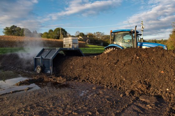 A tractor pulling a compost turner over a pile of dirt.